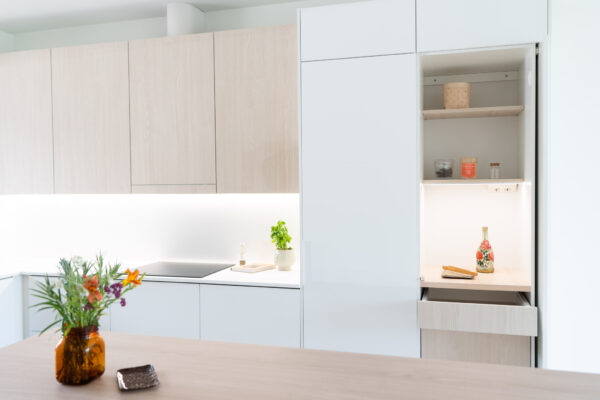 Skandinaavisen vaalea keittiö pocket door -aamiaiskaapilla ja pomppusaranoilla. Kvartetti Saarni -ovet ovat puukuvioitua mikrolaminaattia.
