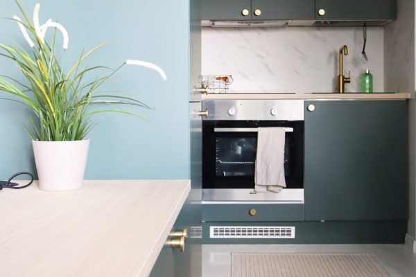 Pienen asunnon yhdistetyssä olotila-keittiössä tummanvihreät Zenit Luxe -kalusteovet ja messinkiset vedinnupit
