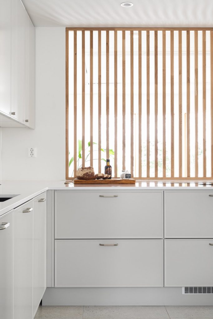 Syvä keittiöniemeke ja valoa lävistävä rimoitus harmaassa Unique Home -keittiössä.