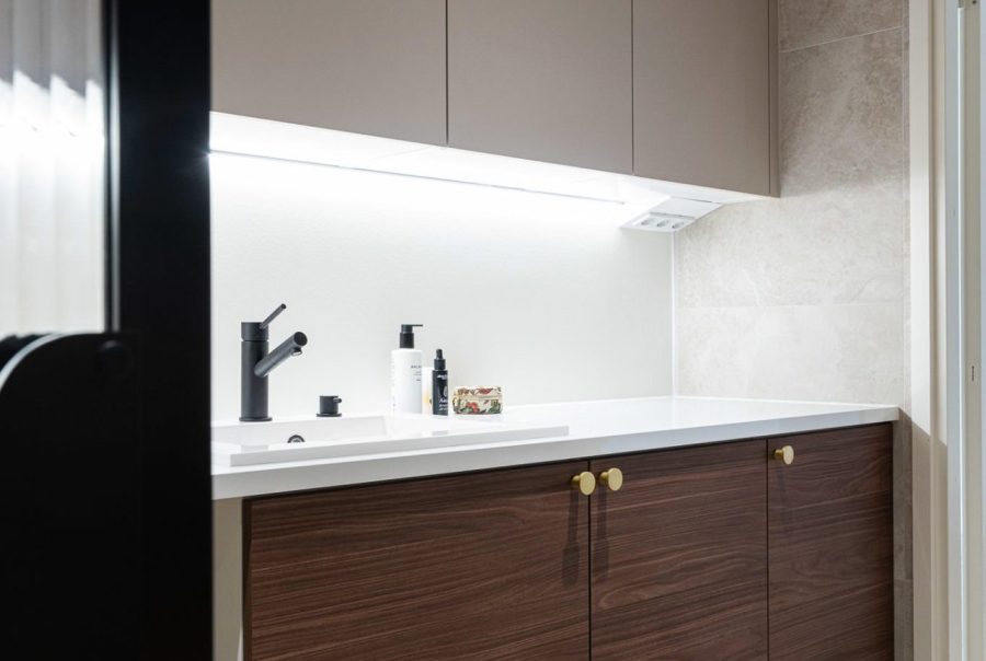 Tyylikäs kodinhoitopiste kylpyhuoneen yhteyteen syntyi kaksivärisillä kaapistoilla.