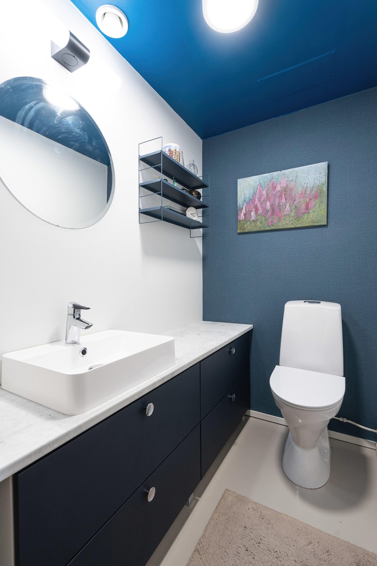Tummansininen allaskaluste, vaalea laminaattitaso sekä malja-allas luovat tämän wc-tilan kalustekokonaisuuden.
