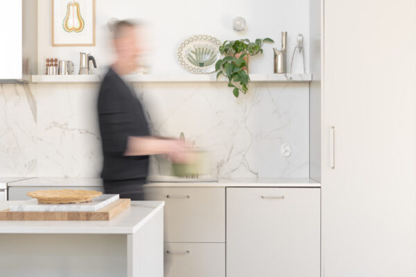 Vaaleanharmaassa avokeittiössä on reilusti tilaa kokkailuun. Dekton-taso materiaali nousee tasoilta näyttävästi välitilaan ja toistuu myös avohyllyssä.