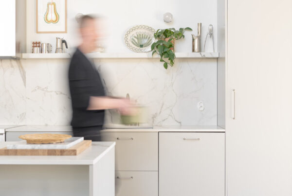 Vaaleanharmaassa avokeittiössä on reilusti tilaa kokkailuun. Dekton-taso materiaali nousee tasoilta näyttävästi välitilaan ja toistuu myös avohyllyssä.