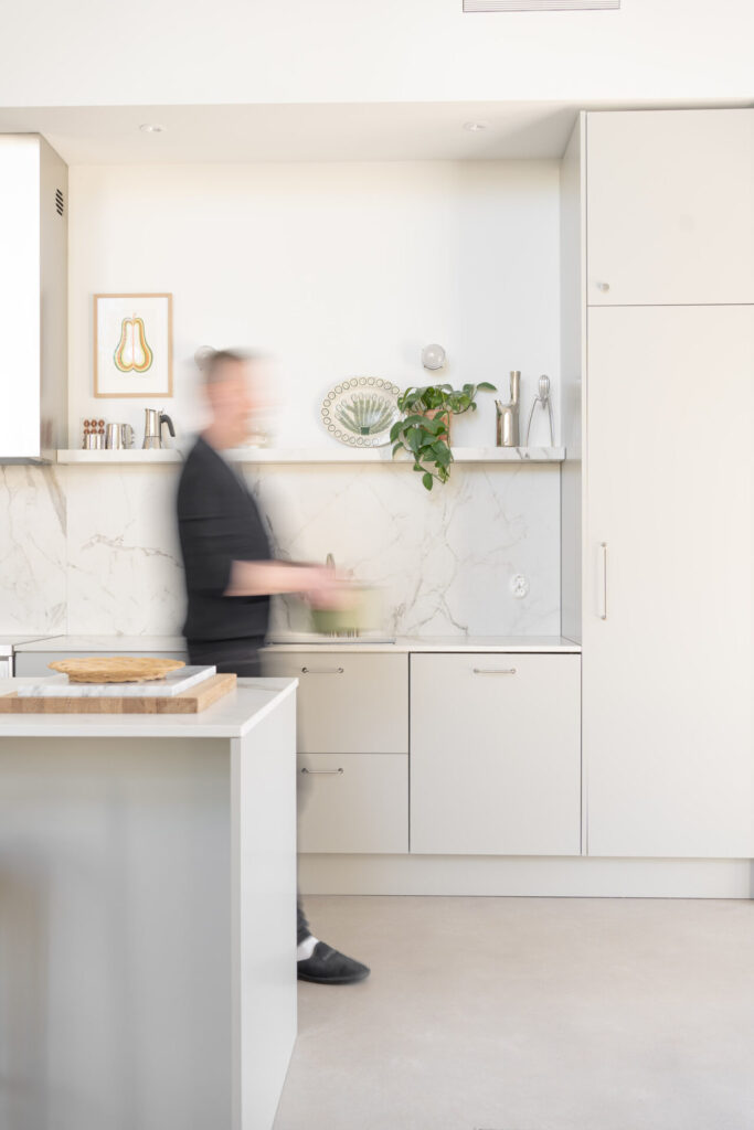 Vaaleanharmaassa avokeittiössä on reilusti tilaa kokkailuun. Dekton-taso materiaali nousee tasoilta näyttävästi välitilaan ja toistuu myös avohyllyssä.